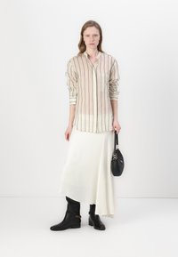 Cream striped button-up shirt with long sleeves, paired with a flowing white skirt and black knee-high boots. Holding a small black handbag.