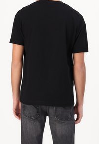 Černé bavlněné tričko s krátkými ohrnutými rukávy, volnější střih a hladký zadní díl. Spárováno s tmavě šedými denimovými džíny.