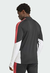 Sort atletisk top med hvide og røde accenter, med lange ærmer og en krave. Fremstillet af glat, strækbart stof.