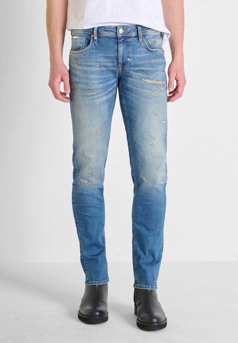 Jeans in denim azzurro chiaro con una vestibilità slim, caratterizzati da toppe strappate, una leggera scoloritura e un classico design a cinque tasche. Abbinati a stivaletti neri.