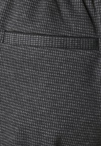 Gråtexturerad tyg med ett hundtandsmönster har en sydd ficka och en slät accentrand längs den övre kanten.