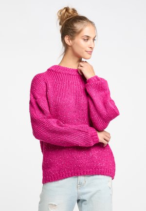 Felroze chunky brei sweater met een geribbeld ontwerp, brede mouwen en een ronde halslijn, gecombineerd met lichtblauwe distressed jeans.