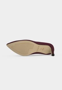 Chaussure à talon haut bordeaux à bout pointu affichée semelle vers le haut, montrant une semelle beige avec grip texturé et marquage de taille 4½.