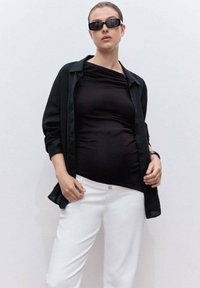 Una maglietta nera a maniche lunghe sopra un top nero aderente, abbinata a pantaloni bianchi. L'outfit presenta una texture liscia e un design minimalista.