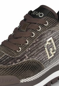 Sneaker marrone con texture in paillettes, design con lacci, dettagli argento e logo; presenta una robusta suola in gomma con una sovrapposizione in rete.