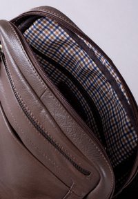 Brown leather bag with a textured exterior. Interior features a checkered fabric lining in blue and brown with additional zippered compartments.