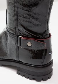 Czarny lakierowany botek z teksturowanym wykończeniem, z czerwonym paskiem i srebrnymi elementami ozdobnymi oraz wytrzymałą czarną podeszwą.