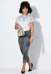 Top corto de manga corta de color dorado metálico, leggins grises con estampados y detalles; modelo sosteniendo un bolso dorado, llevando tacones altos negros.
