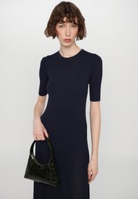 Abito a coste di colore blu navy con maniche corte, abbinato a una borsa nera con motivo croccante e manico curvo. Tessuto liscio e design aderente.