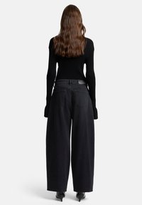 Zwarte wijde jeans met hoge taille, voorzien van minimale achterzakken en een gladde textuur, gecombineerd met een aansluitende zwarte geribbelde trui.