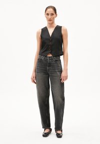 Schwarze Weste mit V-Ausschnitt und drei braunen Knöpfen, kombiniert mit grau-hochgeschnittenen Jeans aus Denim. Die Jeans haben einen lockeren Schnitt und eine leichte Denim-Struktur.