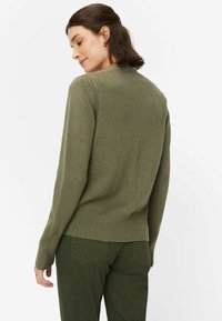 Olivengrüner Strickpullover mit Rundhalsausschnitt, gerippten Bündchen und Saum. Getragen mit passenden olivenfarbenen Hosen, die eine lässige Passform zeigen.