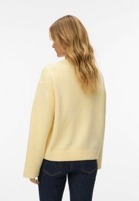 Pull tricoté jaune clair avec un col rond et des poignets côtelés, porté sur un denim foncé, montrant une coupe décontractée et une texture lisse.