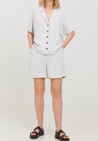 Completo due pezzi in lino grigio chiaro composto da una camicia a maniche corte con bottoni e pantaloni a corto abbinati; bottoni scuri e design comodo.