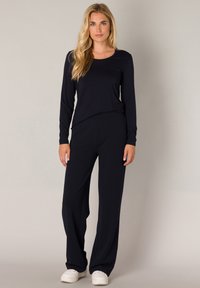 Marineblauw langetermijn top met een ronde hals, gecombineerd met bijpassende brede broek, beide gemaakt van zacht materiaal. Witte sneakers maken de outfit compleet.