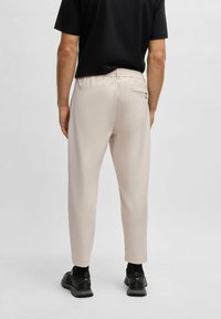 Beige broek met een relaxed fit, elastische tailleband en een achterzak met rits. Draag het met een zwart T-shirt met korte mouwen en sneakers.