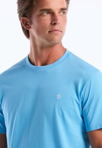 T-shirt bleu clair à manches courtes en coton doux. Il présente un petit logo de pingouin brodé sur le côté gauche de la poitrine. Encolure classique.