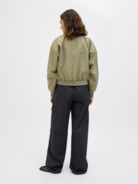 Olive green cropped bomber jacket with elastic waist, paired with baggy black cargo pants featuring side pockets and a textured fabric.