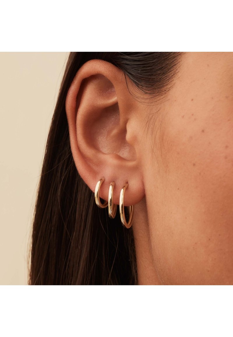 Boucles d'oreilles créoles en métal doré, présentant trois tailles graduées, avec une finition polie, exposées sur une oreille.