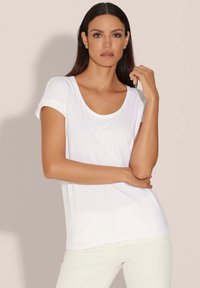 Witte t-shirt met korte mouwen en een ronde hals, gemaakt van soepele stof. Het heeft opgerolde mouwen en een relaxed fit, gecombineerd met lichte broeken.