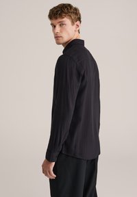 Must värvi pika varrukaga särk, millel on peen triibuline muster, klassikaline krae ja nööbitavad mansetid. Kangas näib sile ning sobib hästi kehasse.