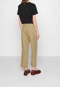 Black short-sleeve cropped t-shirt, khaki wide-leg pants with two back pockets, and brown slip-on shoes, viewed from the back.