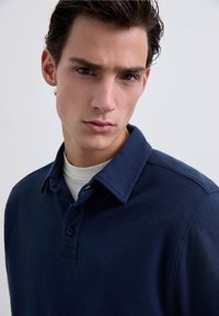 Polo de color azul marino hecho de tejido texturizado, con un collar clásico, tapeta de botones y una silueta ajustada.