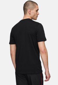 Svart t-shirt med kort ärm, rund halsringning, i bomullsmaterial, med en enkel design utan synliga logotyper eller mönster. Bakvy visas.