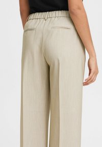 Beige wide-leg trousers featuring a textured fabric, elastic waistband, and two back pockets with simple stitching detail.
