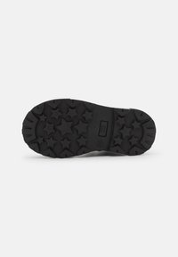 Suela de zapato de goma negra con un patrón de rodadura en forma de estrella, que presenta surcos profundos y una superficie plana para mejorar la tracción. Destacada con el logotipo de la marca.