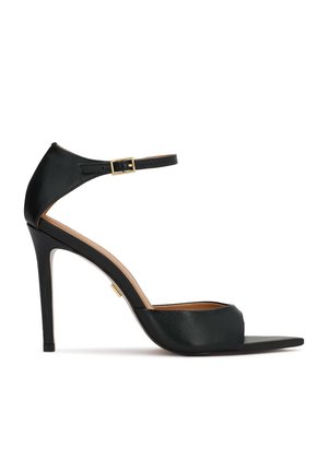 Must nahktakiga sandaal pahklukke rihmaga ja kuldse pandlaga, avatud varbaga ning õhukese kontsaga, valgel taustal.