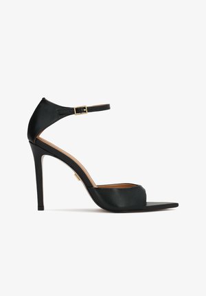 Must nahktakiga sandaal pahklukke rihmaga ja kuldse pandlaga, avatud varbaga ning õhukese kontsaga, valgel taustal.