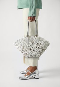 Bolso tote cortado con láser en blanco, con bordes en forma de olas, herrajes plateados y dos asas. Destacado con zapatos de tacón en bloque plateados metálicos.