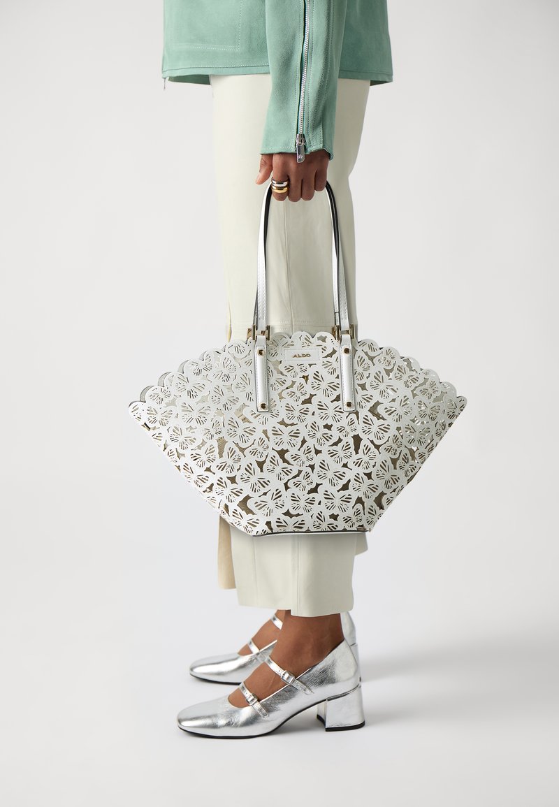 Bolso tote cortado con láser en blanco, con bordes en forma de olas, herrajes plateados y dos asas. Destacado con zapatos de tacón en bloque plateados metálicos.