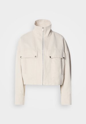 Korte beige jas van katoen met een hoge kraag, een ritssluiting aan de voorkant en twee borstzakken met drukknopen.