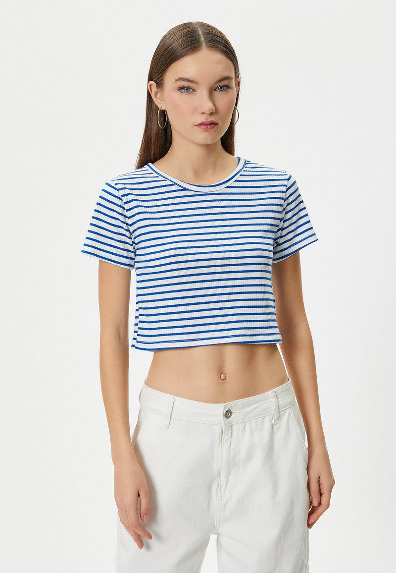 Vit kortärmad T-shirt med blå horisontella ränder, ribbad textur, rund halsringning, korta ärmar, matchad med vita byxor.