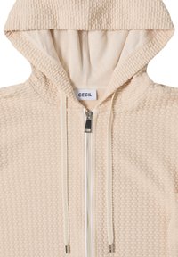 Beige hoodie met ritssluiting, gemaakt van een gestructureerde stof, voorzien van een capuchon en contrasterende trekkoorden. Heeft een metalen rits en een label met de merknaam "CECIL".