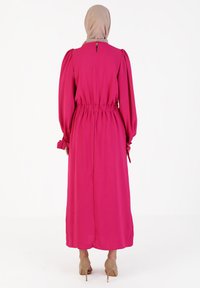 Fuchsia long-sleeve dress with a cinched waist and bow details on the sleeves, featuring a keyhole opening at the back. Smooth fabric texture.