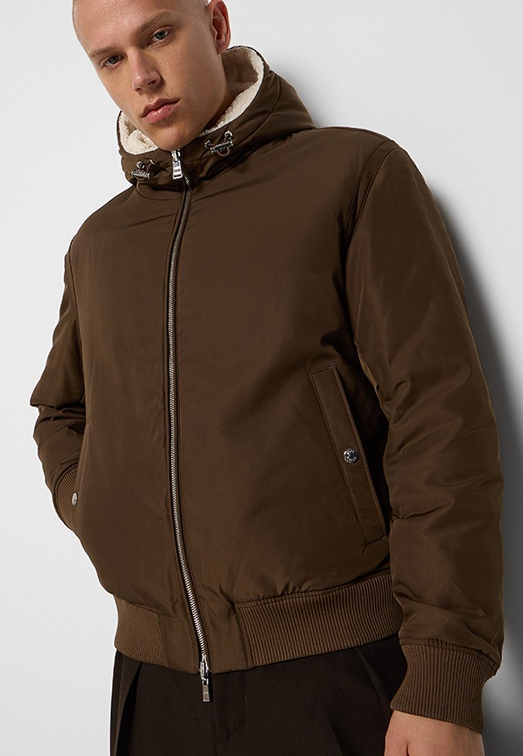 Veste matelassée marron avec fermeture éclair à l'avant, capuche détachable et doublure en polaire. Poignets et ourlet côtelés, avec poches latérales et texture lisse.