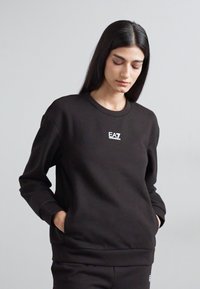 Felpa nera con scollo tondo e maniche lunghe. Presenta un piccolo logo EA7 sul petto. Il materiale sembra morbido e liscio.