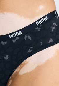 Crne gaćice s uzorkom leopard printa u tamno sivoj boji. Imaju crni elastični pojas s bijelim "PUMA" brandingom. Glatka tekstura.