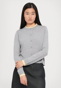 Cardigan grigio chiaro con scollatura tonda, caratterizzato da sette bottoni sul davanti e polsini gialli a contrasto. Texture lavorata a maglia; design aderente.