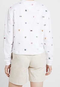 Vit sweatshirt med flerfärgade broderade lappar i olika former och storlekar, med avslappnad passform och ribbad mudd.