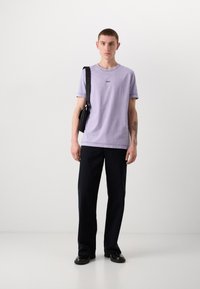 Sarkans lilac krūšu apkakles T-krekls ar izšūtu logotipu, saskaņots ar tumšiem taisnām kājām biksēm un melnām kurpēm, ar mazu plecu somu.