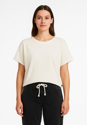 Kurzärmeliges, cremefarbenes Ripp-T-Shirt mit Rundhalsausschnitt, kombiniert mit schwarzen Jogginghosen mit Kordelzug aus strukturiertem Stoff.