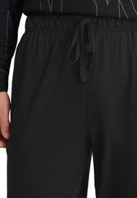 Pantalons de survêtement noirs en tissu doux avec une taille élastique et un cordon de serrage. Présente une coupe décontractée, sans motifs ni accents visibles.