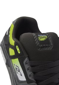 Black and neon green sneaker with mesh upper, rubber sole, padded collar, and logo tag. Textured accents and lace-up design.