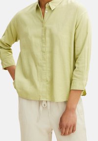 Camicia bottonata verde chiaro con colletto, maniche lunghe arrotolate fino ai gomiti e vestibilità comoda, realizzata in un tessuto morbido e strutturato.