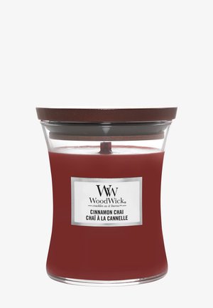 Rød WoodWick kanel chai duftlys i et klart buet glas med mørkt træ låg og etiket med teksten "knitrer, når det brænder."