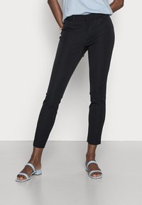 Pantalon noir slim en tissu stretch, avec une texture lisse et une taille standard. Accompagné de sandales à talons bleu clair.
